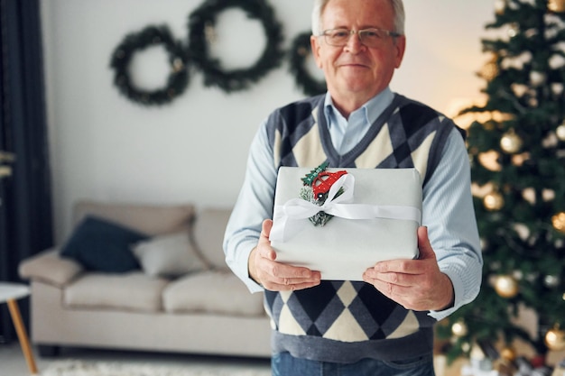 Celebrando el año nuevo y de pie cerca del árbol de navidad Un hombre mayor con ropa bonita está en casa