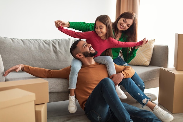 Celebrando el día de la mudanza. Papá y mamá árabes alegres divirtiéndose con su hijo, jugando en la sala de estar, hija sonriente sentada en el cuello del padre. Familia amorosa feliz disfrutando de pasar tiempo juntos