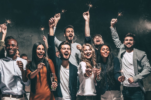 Foto celebrando con diversión. grupo de jóvenes alegres portando bengalas y copas de champán