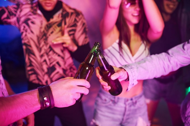 Celebrando y golpeando botellas con alcohol Los jóvenes se divierten en un club nocturno con luces láser de colores