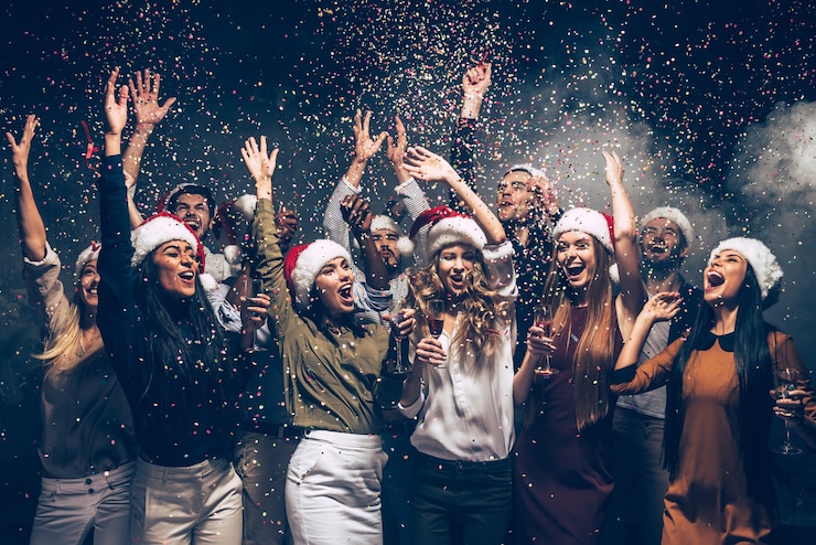 Foto celebrando o ano novo juntos. grupo de jovens lindos com chapéus de papai noel jogando confetes coloridos e parecendo felizes