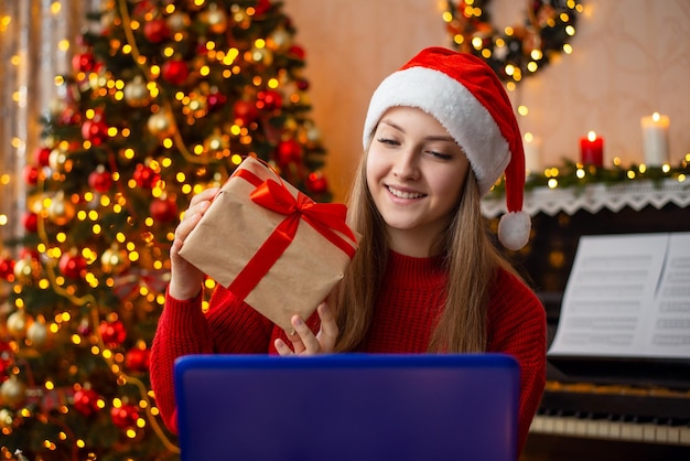 Celebrando o Natal com pessoas próximas online Garota sorridente mostrando presente para a webcam do laptop conversando com uma pessoa via Internet