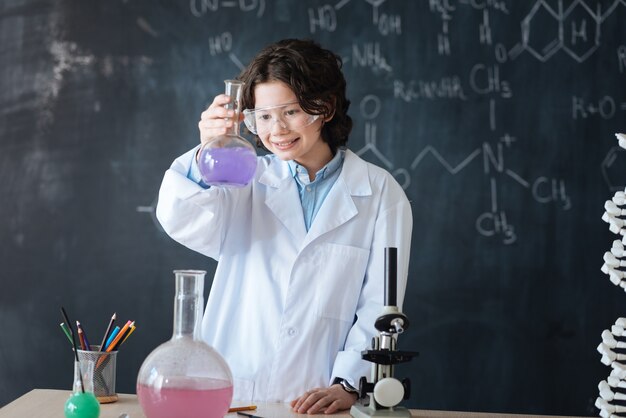 Celebrando los primeros éxitos. Sonriente científico inspirado satisfecho de pie en el laboratorio y disfrutando de la clase de química mientras participa en el proyecto científico y expresa felicidad