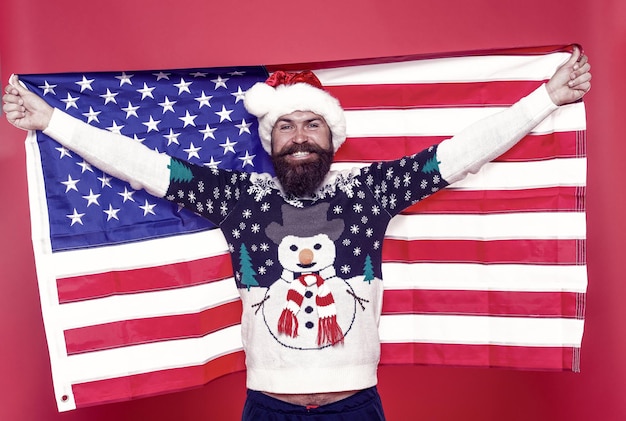 Celebre el estilo americano. El hombre americano barbudo celebra la Navidad. Feliz santa mantenga la bandera americana. Saludos de la estación. Vacaciones de invierno. Víspera de año nuevo. Gran Navidad americana.