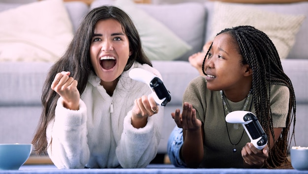 Celebre o controlador e os amigos jogando um jogo na sala de estar para entretenimento, diversão e união Feliz celebração e mulheres inter-raciais desfrutando de uma competição de jogos juntas em sua casa