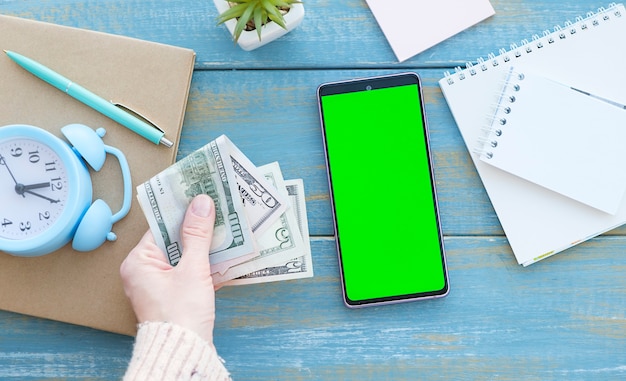 Celular com tela verde em um laptop e dinheiro como fundo de madeira