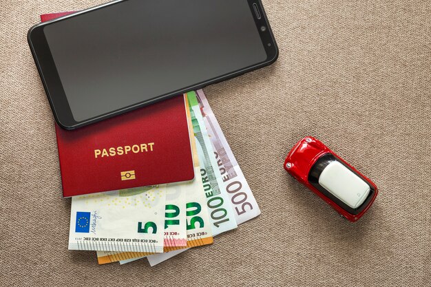 Celular negro, billetes de billetes de dinero en euros, pasaporte y coche de juguete