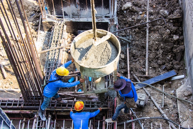 Cemento de colada del trabajador que vierte en encofrado de las fundaciones en el área del edificio en emplazamiento de la obra.