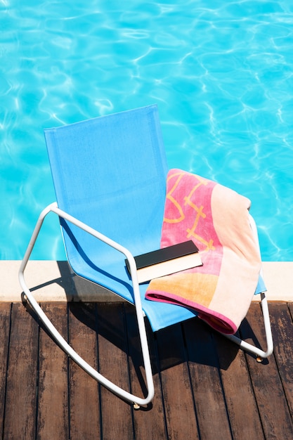 Foto cena da cadeira de sol com toalha de praia e livro na piscina