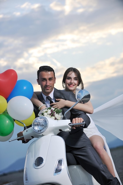 Cena de casamento dos noivos recém-casados na praia andam de scooter branca e se divertem