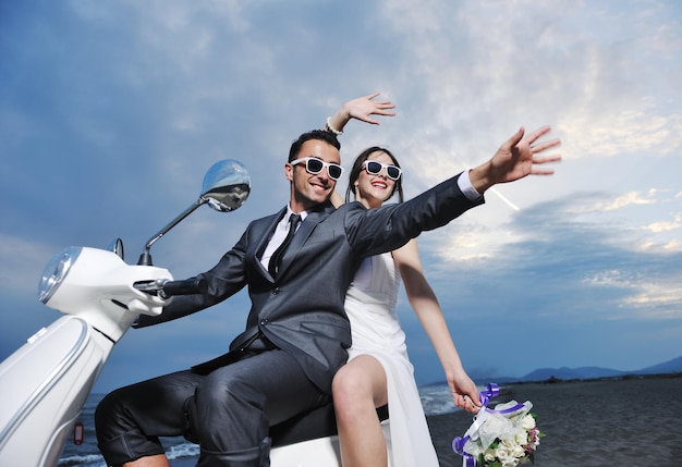 Foto cena de casamento dos noivos recém-casados na praia andam de scooter branca e se divertem
