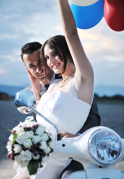 Foto cena de casamento dos noivos recém-casados na praia andam de scooter branca e se divertem