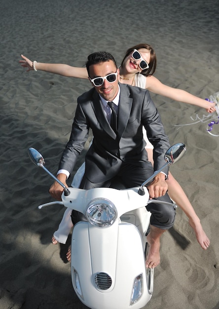 Foto cena de casamento dos noivos recém casados na praia andam de scooter branca e se divertem