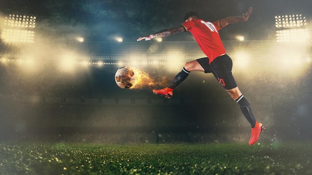 Cena de futebol no jogo noturno com jogador de uniforme vermelho chutando uma bola de fogo com poder
