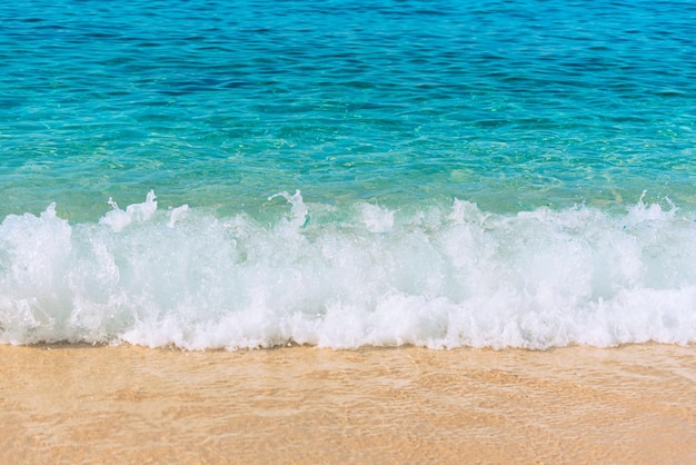 Cena de verão com espuma branca de água do mar azul e areia amarela fechar com foco seletivo Conceito de férias ou férias Fundo da natureza com espaço de cópia