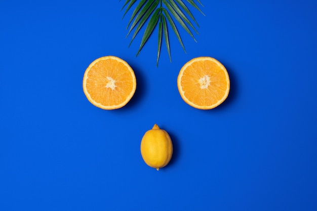 Cena de verão com folha de palmeira tropical, laranja e limão sobre fundo azul. estética mínima. estilo liso leigo. copie o espaço