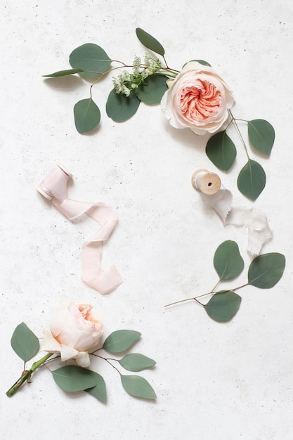 Cena de vida de aniversário de casamento feminino fitas de seda folhas de eucalipto e blush rosas rosas inglesas flores fundo de mesa de concreto vista superior plana layvertical espaço de cópia vazio