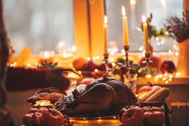Cena del día de Acción de Gracias con decoración navideña de otoño y velas Mesa de comedor familiar con delicioso pavo asado dorado en un plato adornado con calabazas pequeñas frescas y romero