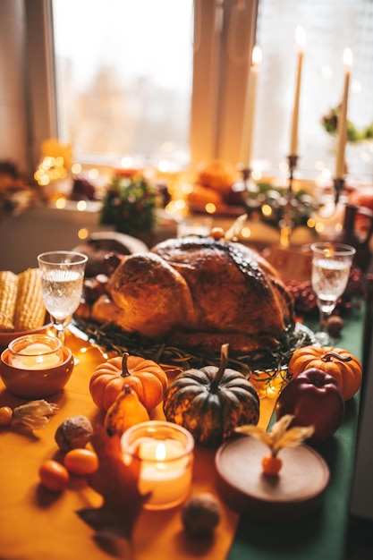 Cena del día de Acción de Gracias con decoración navideña de otoño y velas Mesa de comedor familiar con delicioso pavo asado dorado en un plato adornado con calabazas pequeñas frescas y romero