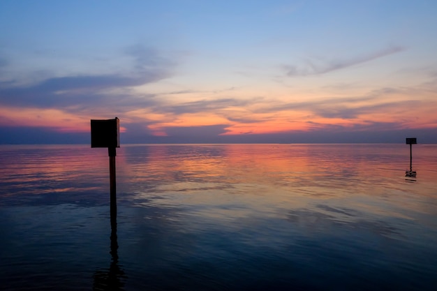 Foto cena do por do sol com o polo de aço de marcação de advertência no mar, tempo crepuscular.