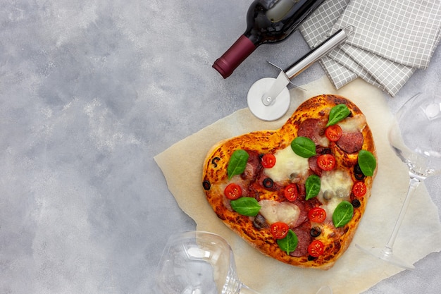 Cena festiva. Pizza de corazón con una botella de vino y vasos