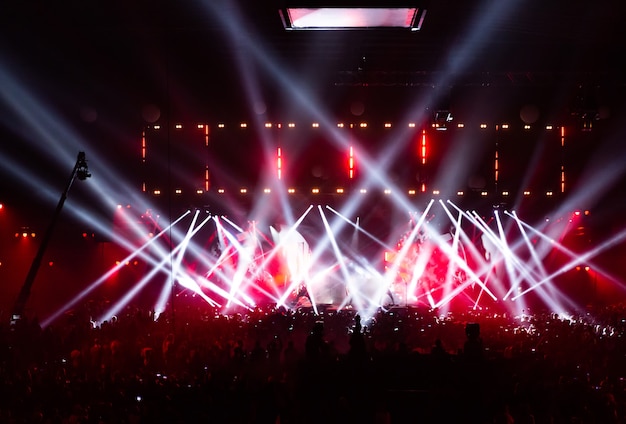 Cena iluminada por belos raios de equipamentos de iluminação. A multidão do show se divertindo no centro do grande salão. A televisão é transmitida ao vivo. Muitas pessoas olham para o palco.