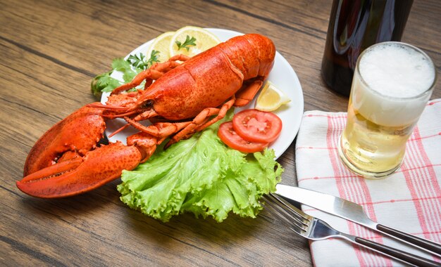 Foto cena de langosta de mariscos cocida al vapor en un plato de mariscos con ensalada de limón, lechuga, vegetales y tomate / cerveza en la mesa