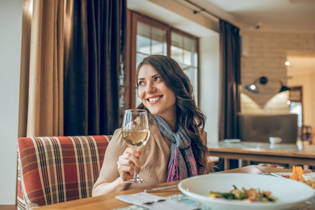 Cena. Linda mujer morena sentada a la mesa en un restaurante y mirando feliz