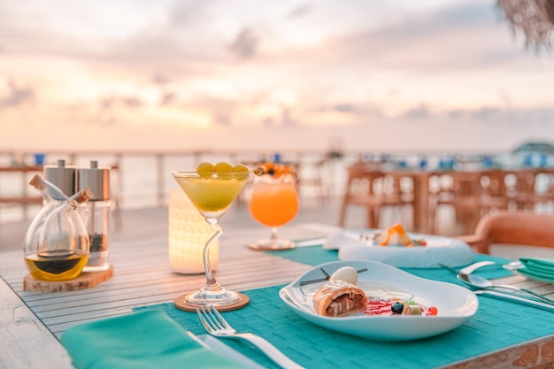 Cena de lujo al atardecer comida gourmet en mesa de madera, hermoso resort tropical y vista al mar, elegante