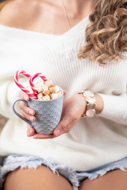 Cena mágica de Natal, ambiente aconchegante. Mulher segurando um copo de bebida com marshmallows.