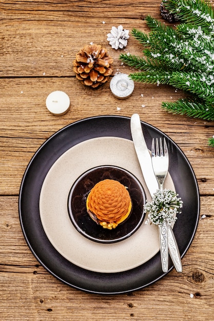 Cena de Navidad y Año Nuevo. Merienda dulce, rama de abeto, velas, conos, platos de cerámica, tenedor y cuchillo.