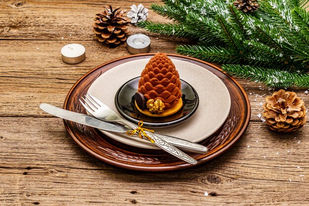 Cena de Navidad y Año Nuevo. Merienda dulce, rama de abeto, velas, conos, platos de cerámica, tenedor y cuchillo.
