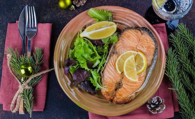 Foto cena de navidad mesa. delicioso filete de salmón a la parrilla en un plato con limón y una variedad de ensalada en la mesa de piedra oscura. vista superior, espacio de copia