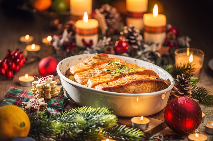 Foto cena de navidad de pescado salmón en un plato para asar con decoración festiva corona de adviento y velas encendidas.