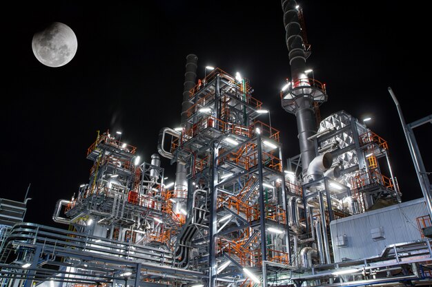 Cena noturna de detalhes de uma planta industrial química pesada com refinaria de tubos em lua cheia ao entardecer