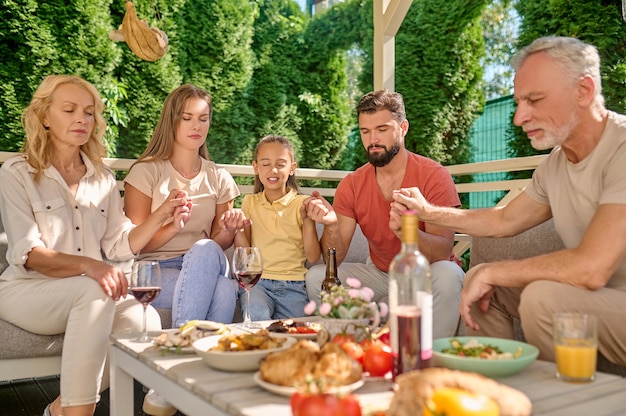 Cena de oración. Una familia sentada con los ojos cerrados y rezando juntos antes de la cena.