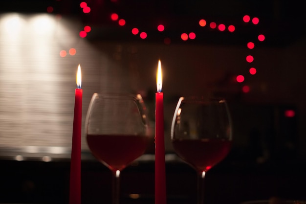 Cena romántica dos copas de vino y velas en la oscuridad con luces de año nuevo al fondo