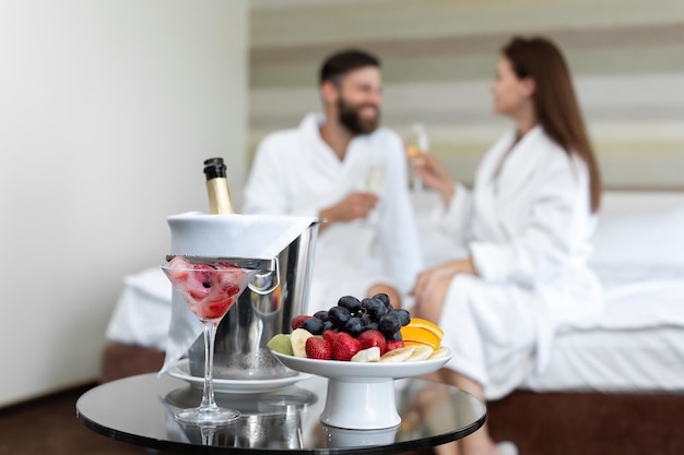 Foto cena romántica en el hotel de bayas y frutas para una pareja joven que bebe champán en la cama