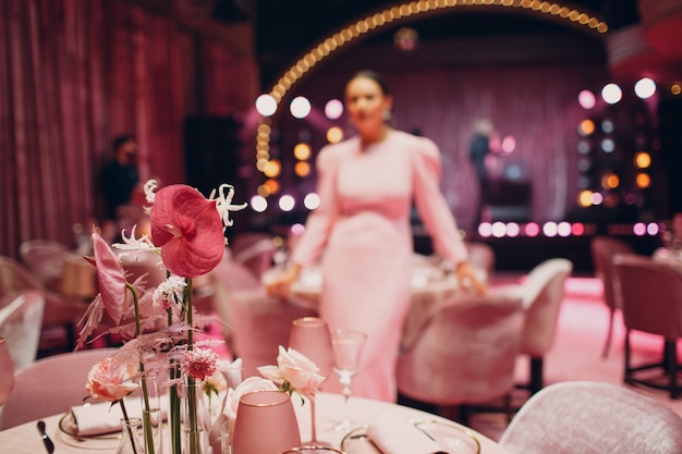Cena romántica mesa de decoración rosa en el restaurante con mowan borrosa en vestido en el fondo