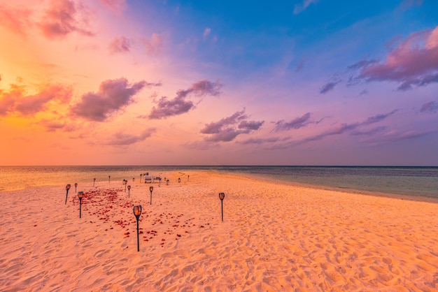 Cena romántica en la playa con velas y antorchas bajo el maravilloso cielo del atardecer. Propuesta de luna de miel en pareja