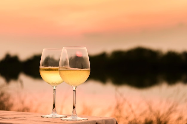 Una cena romántica en verano en una playa al atardecer con dos copas de vino blanco.