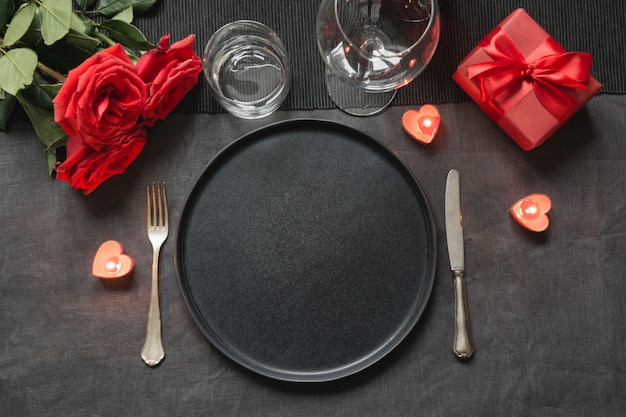 Cena de San Valentín o cumpleaños. El ajuste de la tabla de la elegancia con rojo se levantó en mantel de lino negro.