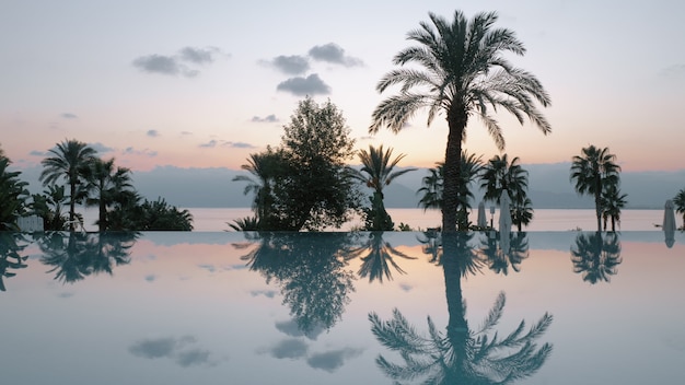 Cena serena de resort ao pôr do sol, piscina e mar com montanhas