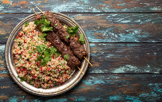 Cena turca del Medio Oriente con kebab de carne y ensalada de cuscús tabbouleh en placa de metal rústico en la vista superior de fondo de madera con espacio de copia, comida árabe tradicional