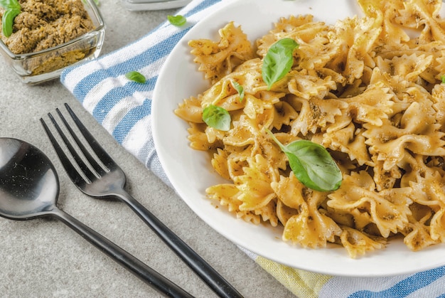 Cena vegana. Farfalle pasta con salsa de pesto y hojas de albahaca sobre placa blanca fondo de piedra gris