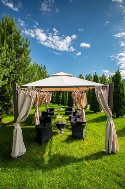 Cenador de lona blanca con muebles de jardín de plástico en un césped verde de verano Espacio de copia vertical