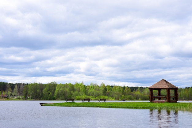 Cenador de picnic con bancos en la orilla de un lago del bosque