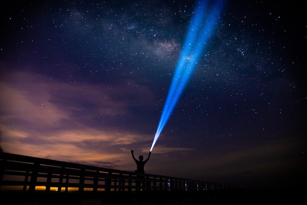 Foto cenário da via láctea, céu noturno estrelado com um homem parado na ponte iluminando uma tocha