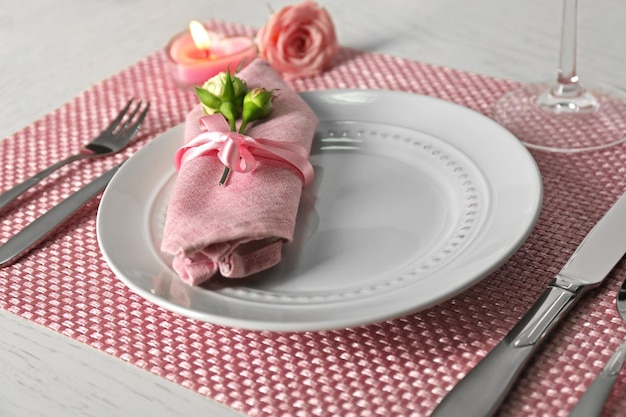 Cenário de mesa com pratos, guardanapos, talheres e velas no fundo rosa