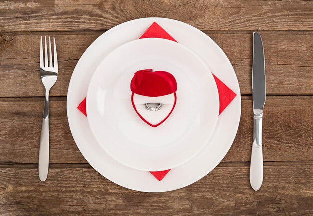 Cenário de mesa de jantar de dia dos namorados com faca e garfo de anel de caixa vermelha sobre fundo de carvalho